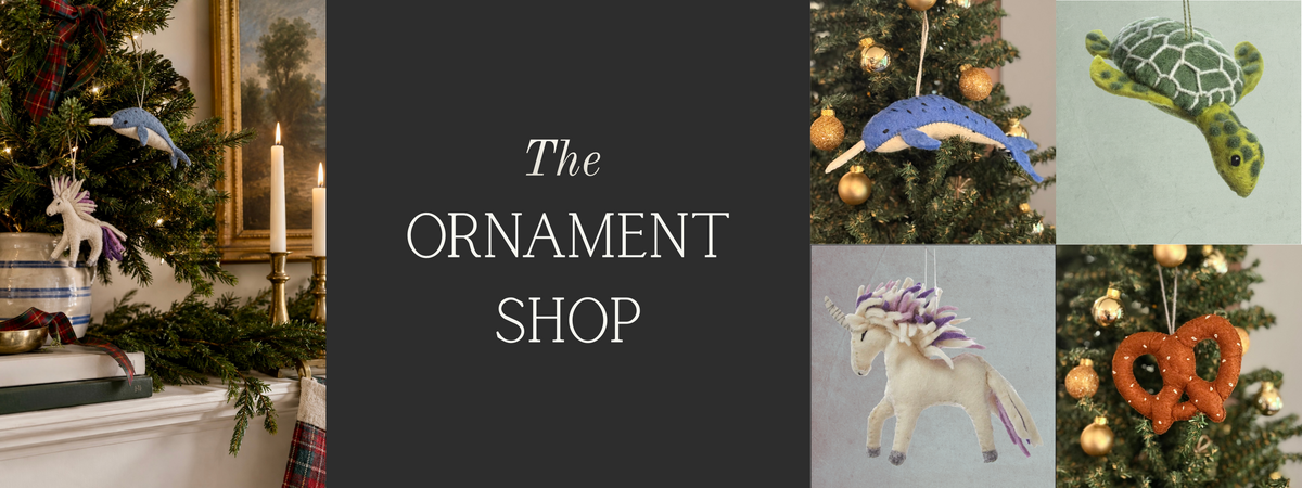 A promotional banner for 'The Ornament Shop' featuring a central dark gray text panel and four surrounding product photos of Christmas ornaments: a blue whale, a green turtle, a white unicorn with purple details, and an orange pretzel-shaped ornament, all displayed on or beside Christmas trees.